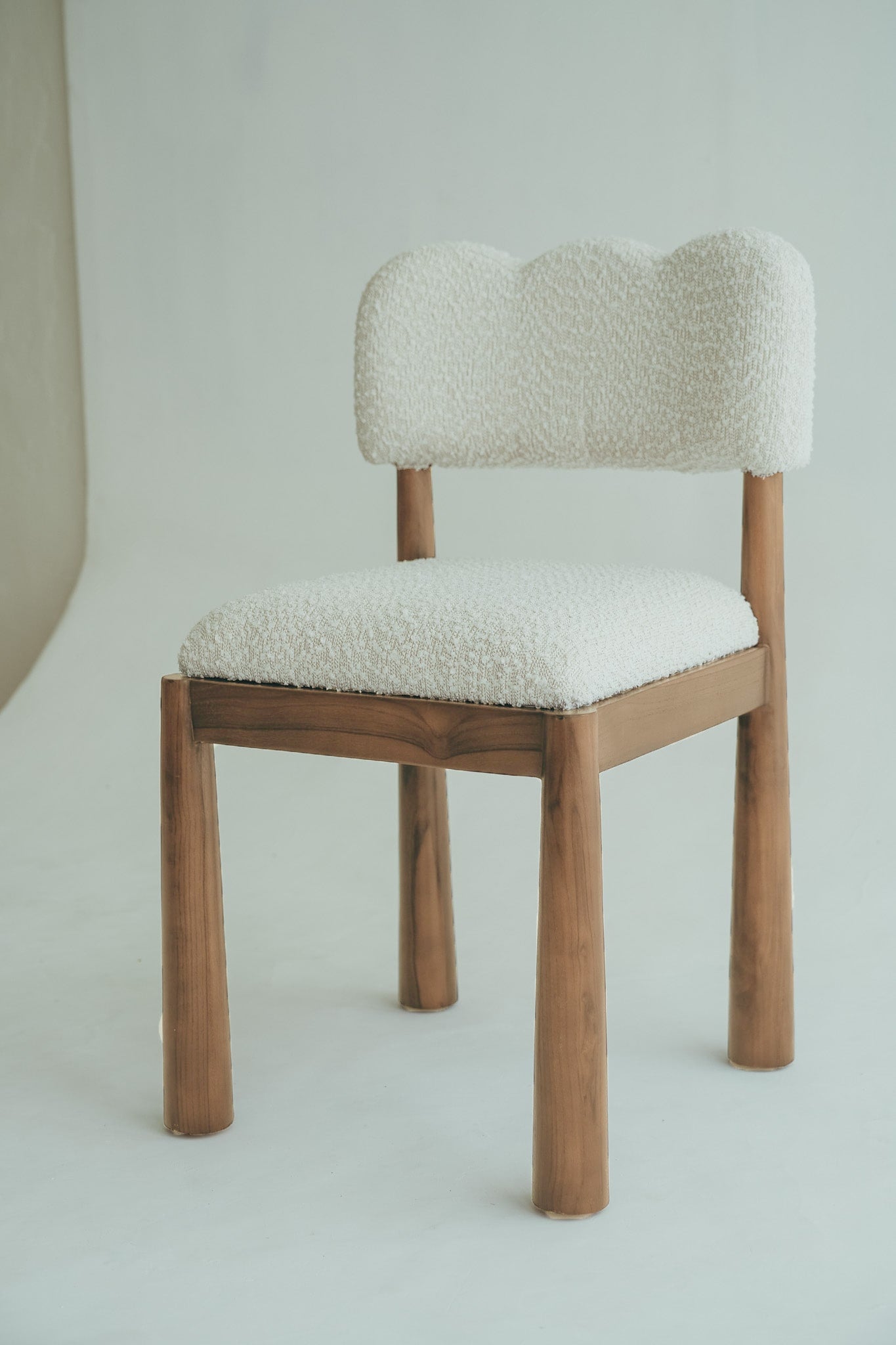 Wavy dining chair made of teak wood with a bouclé fabric seat.
