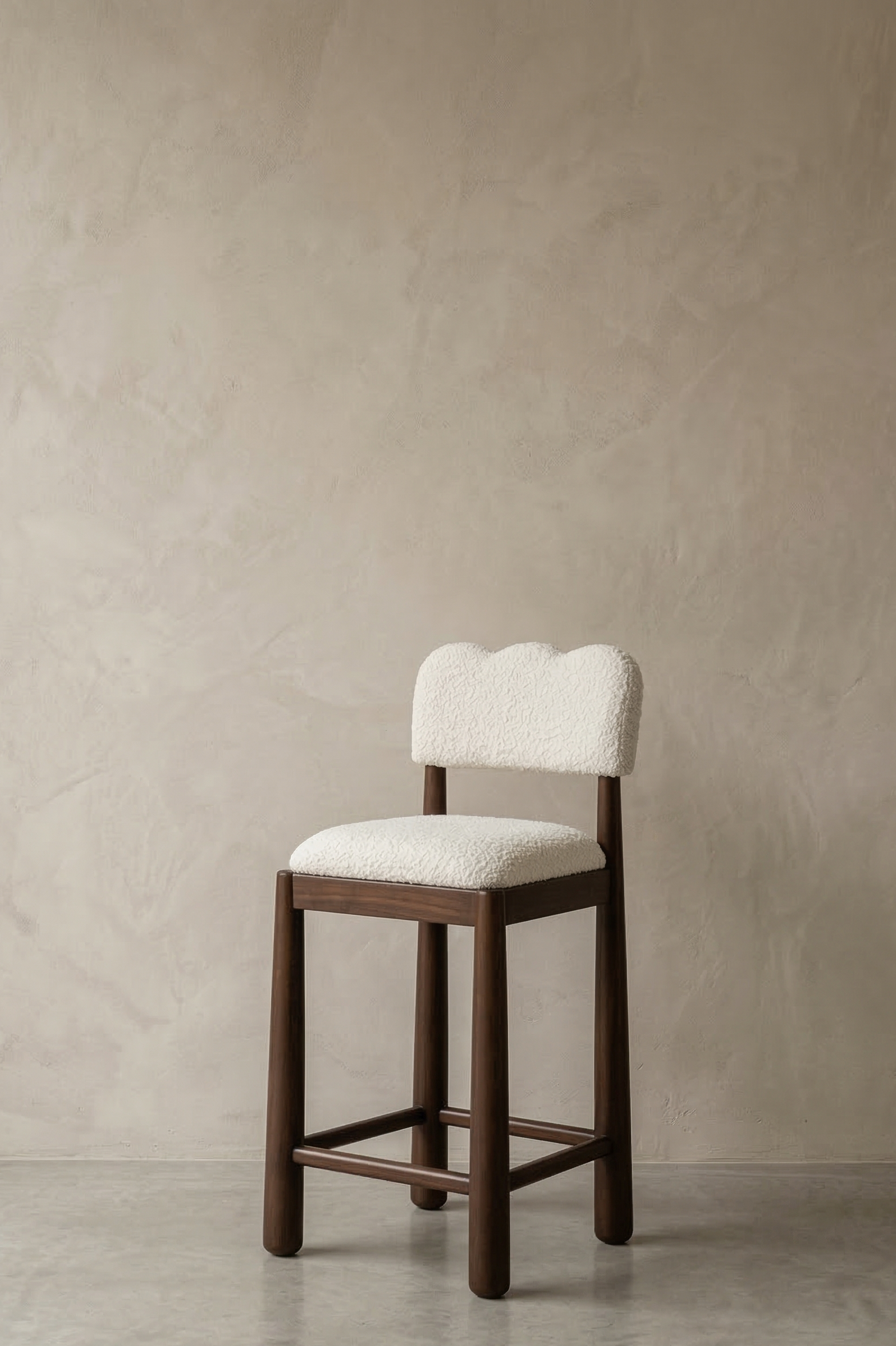 Wooden bar stool with white cushioned seat and backrest against a beige wall.
