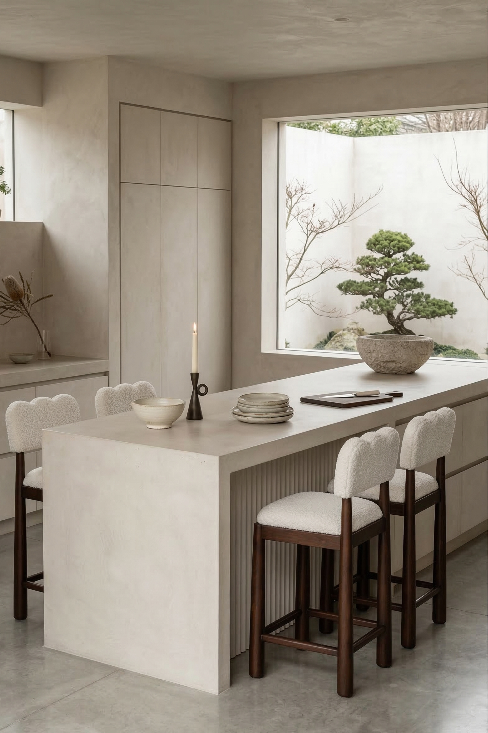 Modern kitchen with a white island and stools, featuring a bonsai tree in the background.