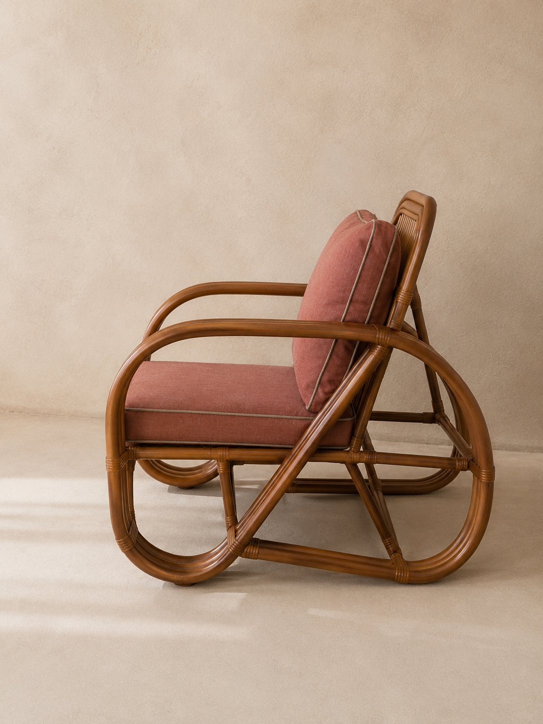 A mid-century modern rattan armchair with curved brown wooden frames and dusty rose pink cushions, set against a warm beige textured wall and floor.