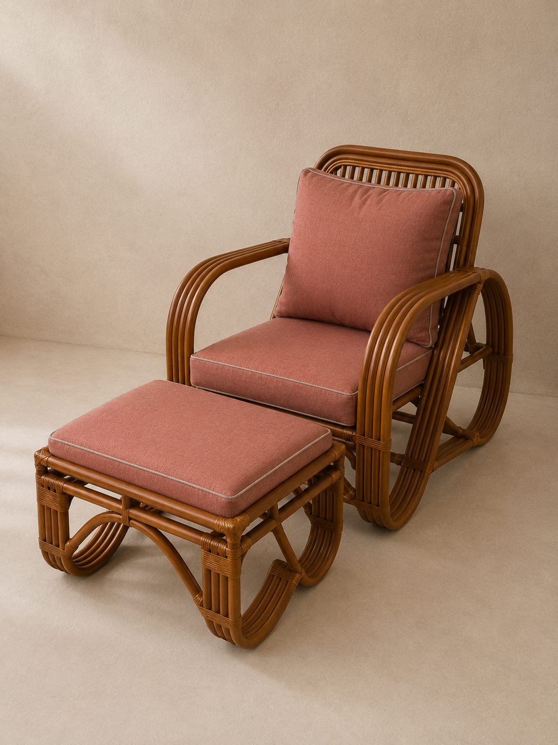 A rattan armchair with a matching ottoman and back cushion in dusty rose pink, set against a warm beige textured studio background.