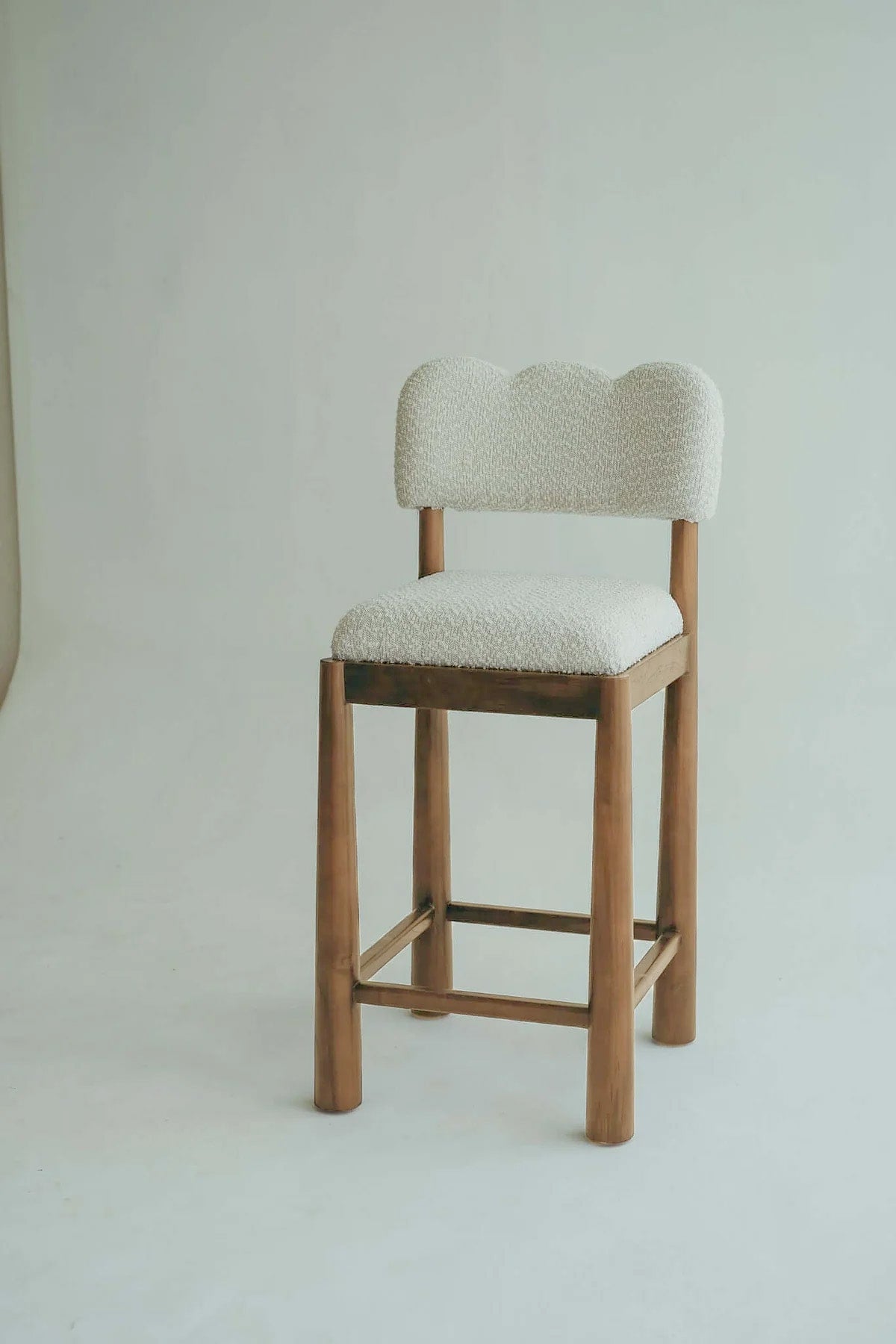 Wavy bar stool chair made of teak wood with a bouclé fabric seat.