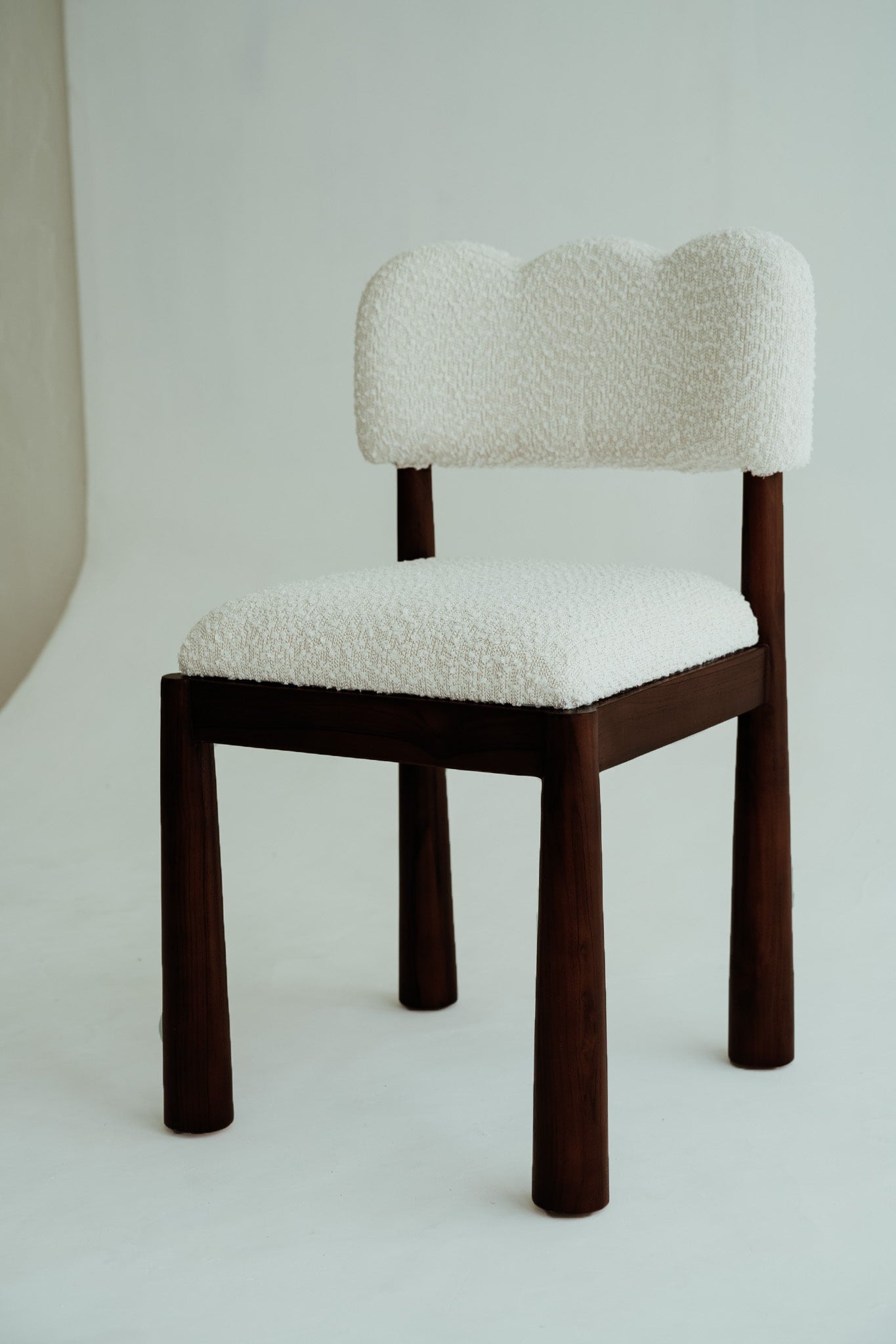 Wavy dining chair made of teak wood with a bouclé fabric seat.